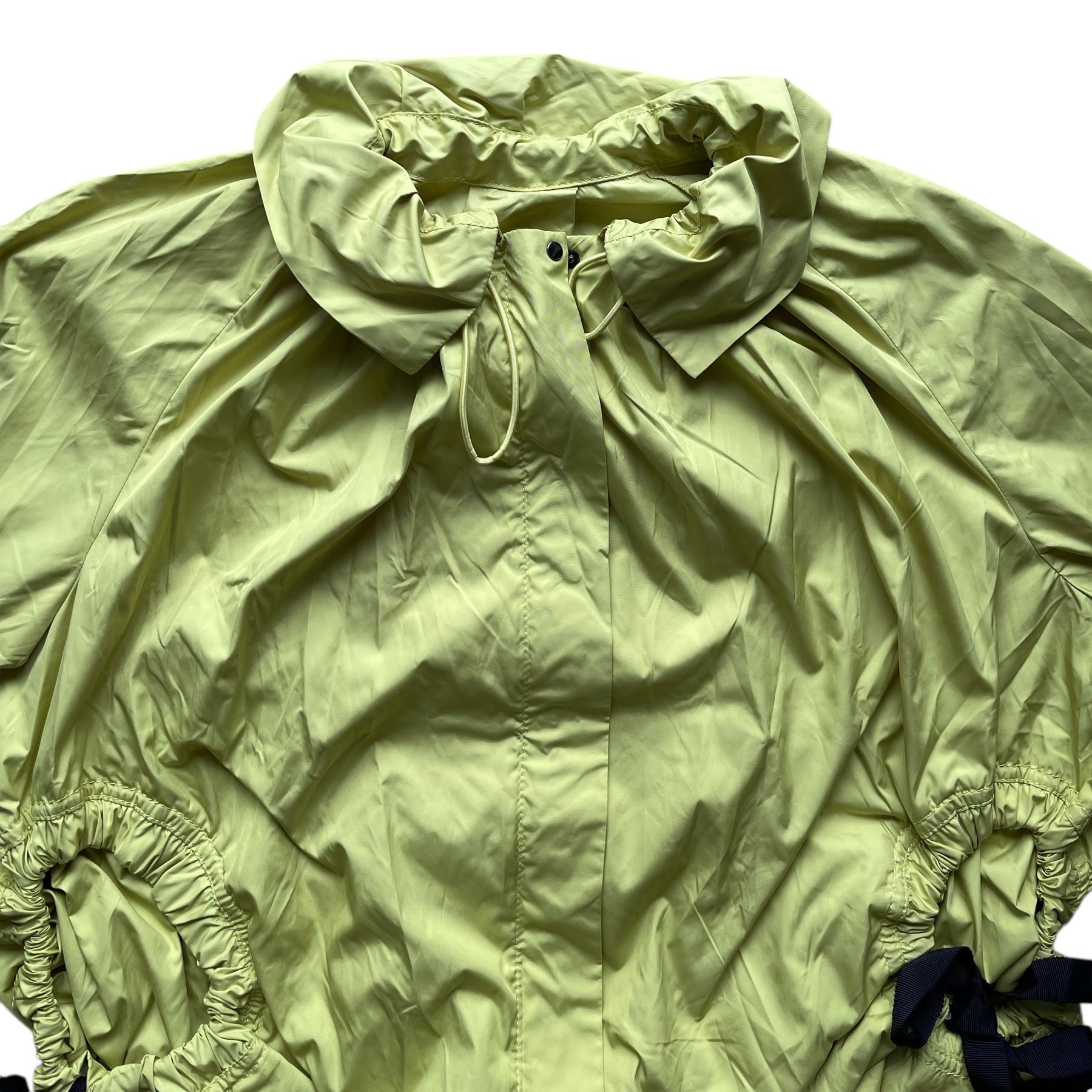Veste coupe-vent vert anis légère avec col montant, manches longues et cordons noirs pour resserrer la taille.