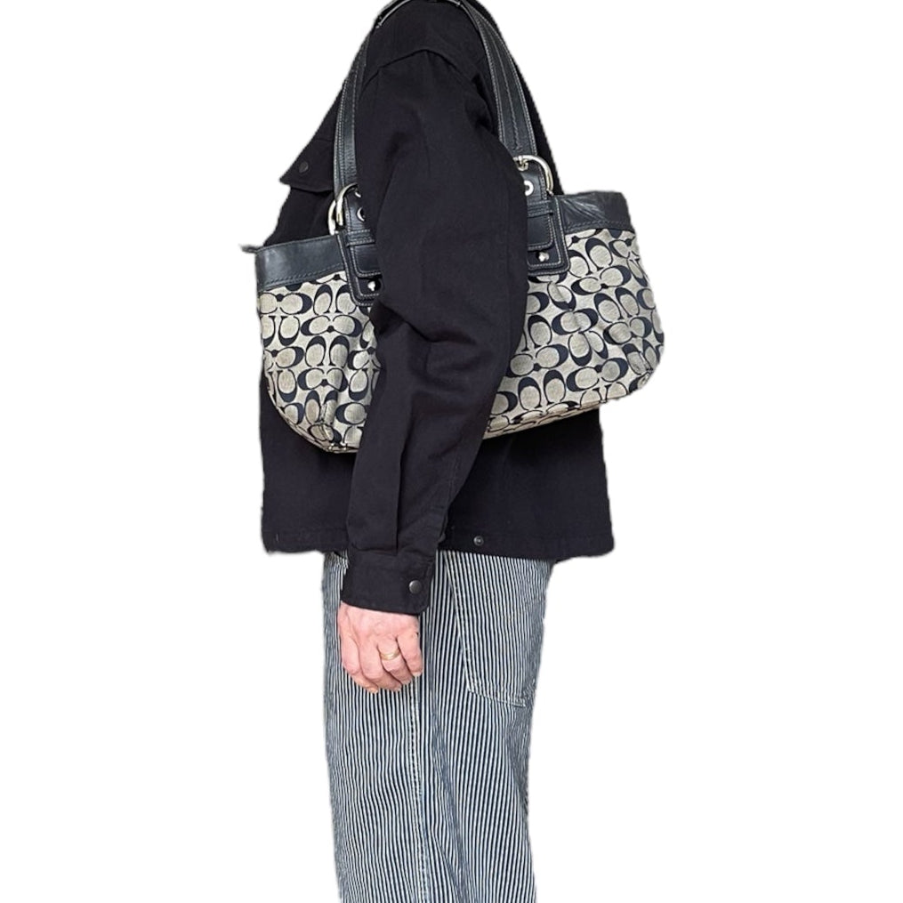 Sac à main Coach vintage en toile monogrammée beige et cuir noir, avec deux anses et boucles argentées, format moyen élégant.